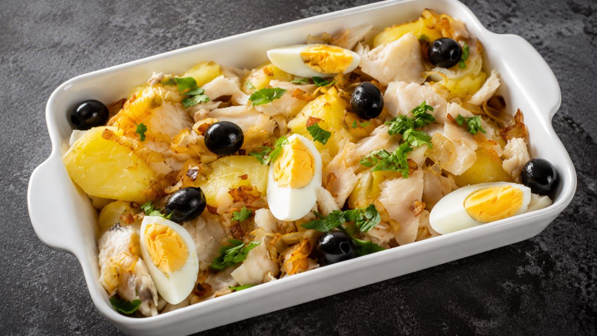 Travessa de bacalhau à Gomes de Sá com lascas de peixe batatas cozidas ovos fatiados azeitonas pretas e salsa.