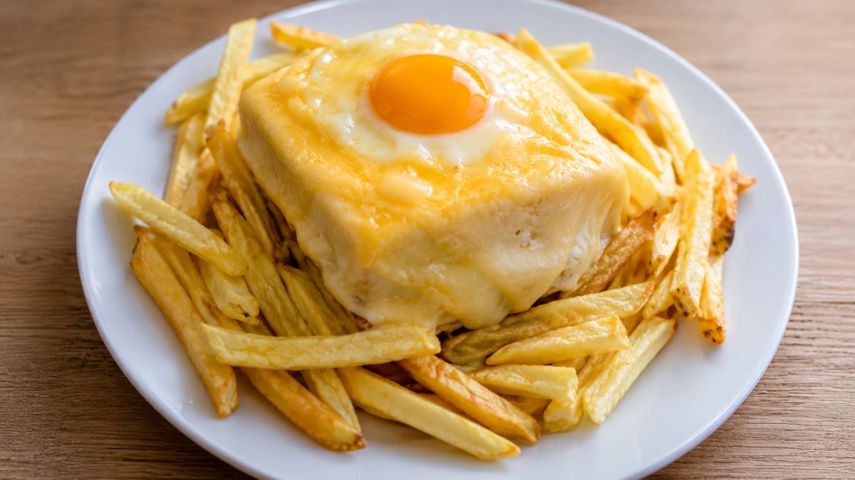 Prato de francesinha tradicional portuguesa com queijo derretido e ovo estalado sobre uma porção de batatas fritas.