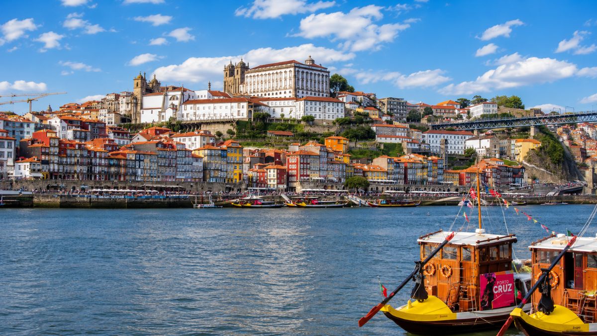 Vista do casario histórico da Ribeira no Porto e barcos rabelos tradicionais ancorados no Rio Douro durante o dia.