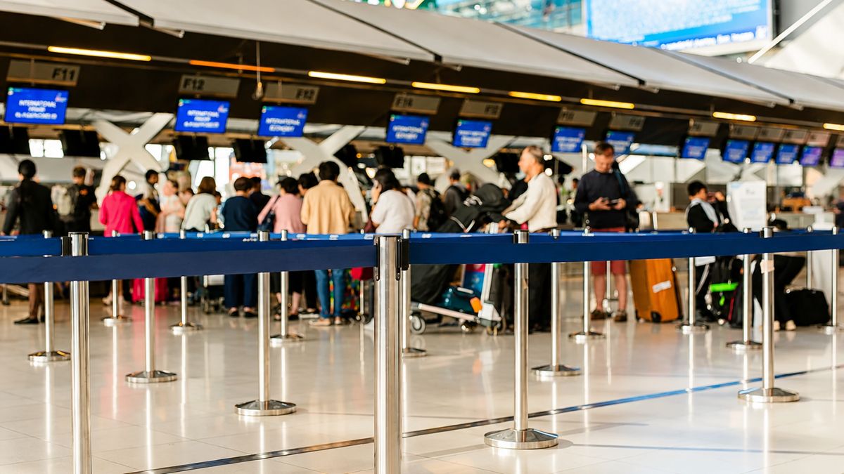 Passageiros aguardam atendimento em filas organizadas nos balcões de check in de um aeroporto moderno, com malas, painéis eletrônicos e ambiente iluminado.