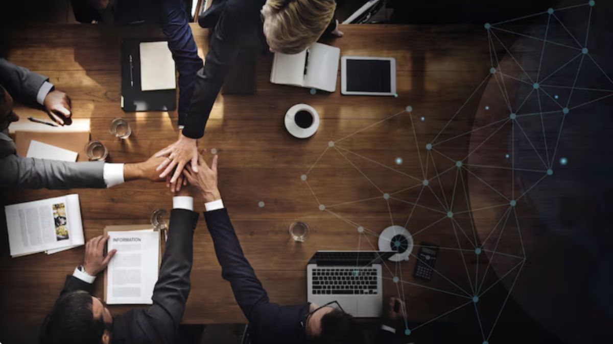 Vista superior de profissionais de negócios reunidos ao redor de uma mesa de madeira, empilhando as mãos no centro, com uma sobreposição gráfica de rede digital conectada no lado direito.