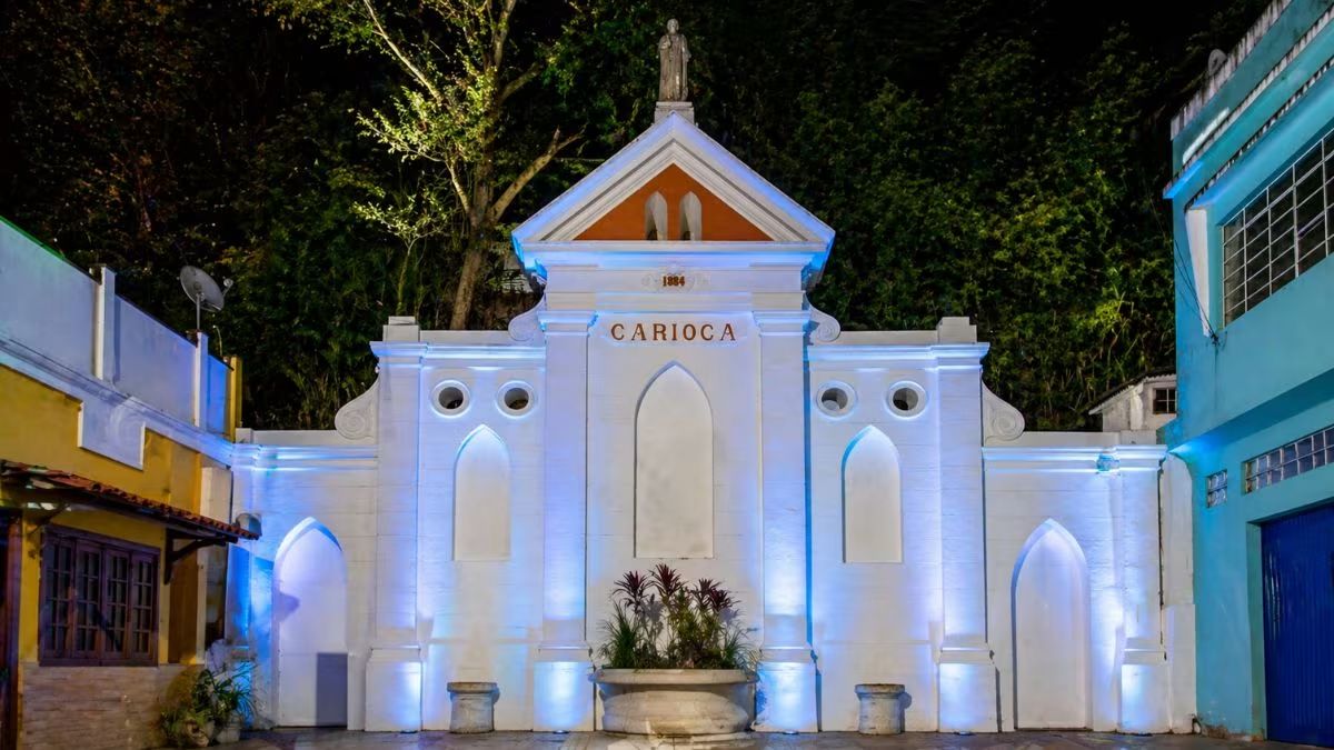 Vista noturna do Chafariz da Carioca em Barra do Piraí com fachada branca iluminação azul estátua no topo e a inscrição 1884.