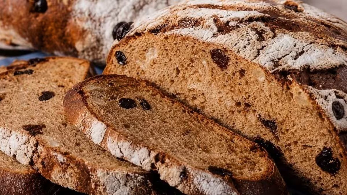 Pão de café artesanal fatiado com casca rústica polvilhada com farinha e miolo macio recheado com uvas passas.