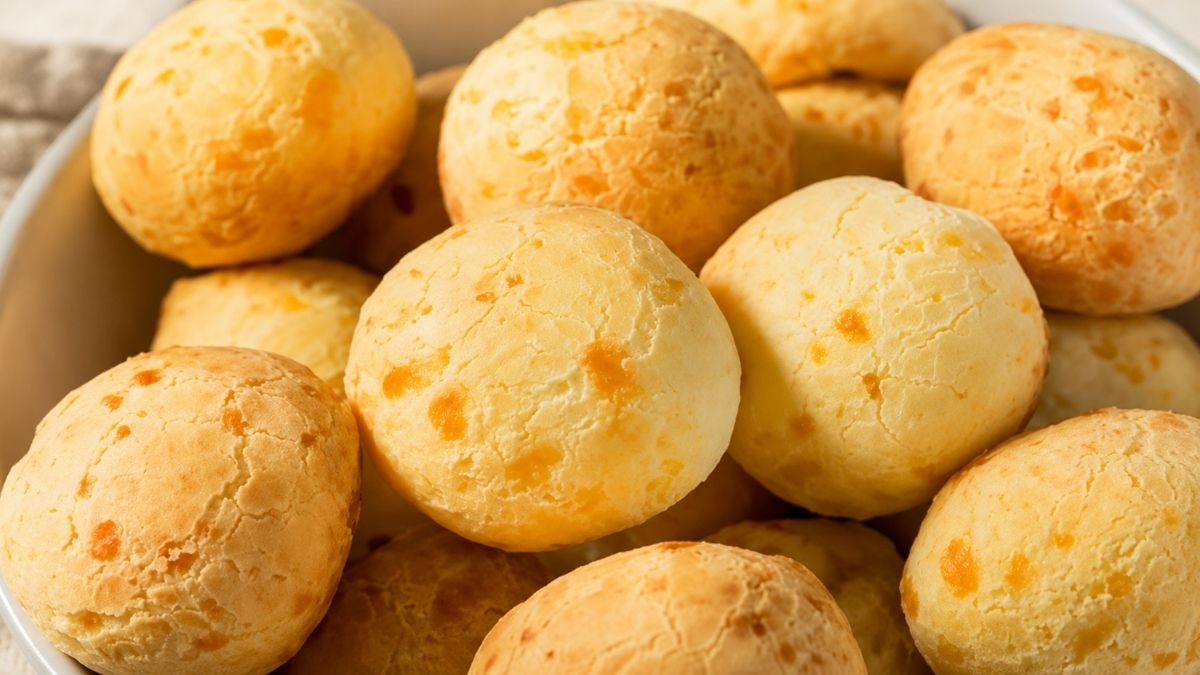 Vários pães de queijo mineiros assados, bem dourados e redondos, servidos juntos em um recipiente, destacando a crosta crocante e o queijo.