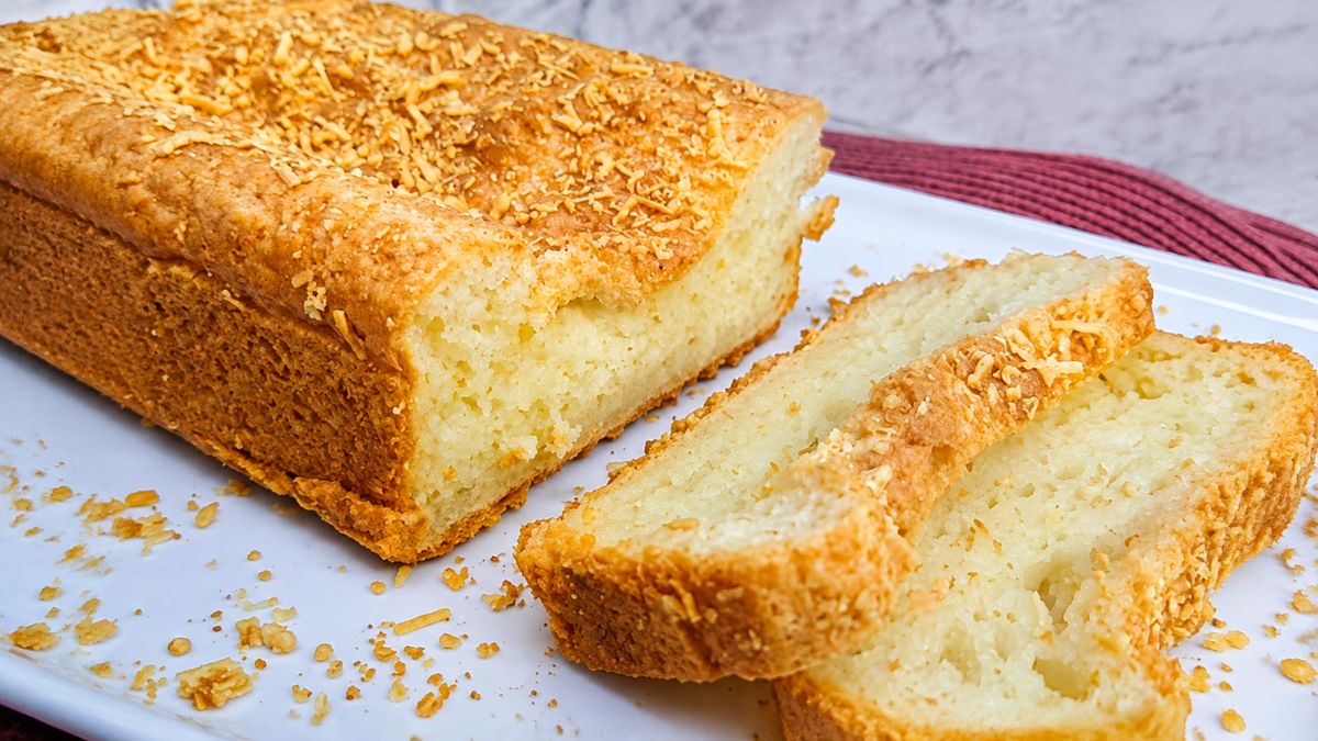 Pão de queijo de forma fatiado em uma travessa branca, mostrando a massa macia, a casca dourada e o queijo ralado gratinado por cima.