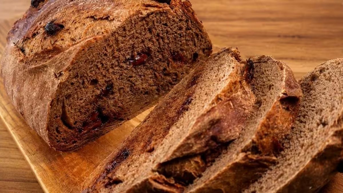 Pão de cacau artesanal fatiado com miolo macio e pedaços de chocolate escuro sobre uma tábua de madeira rústica.